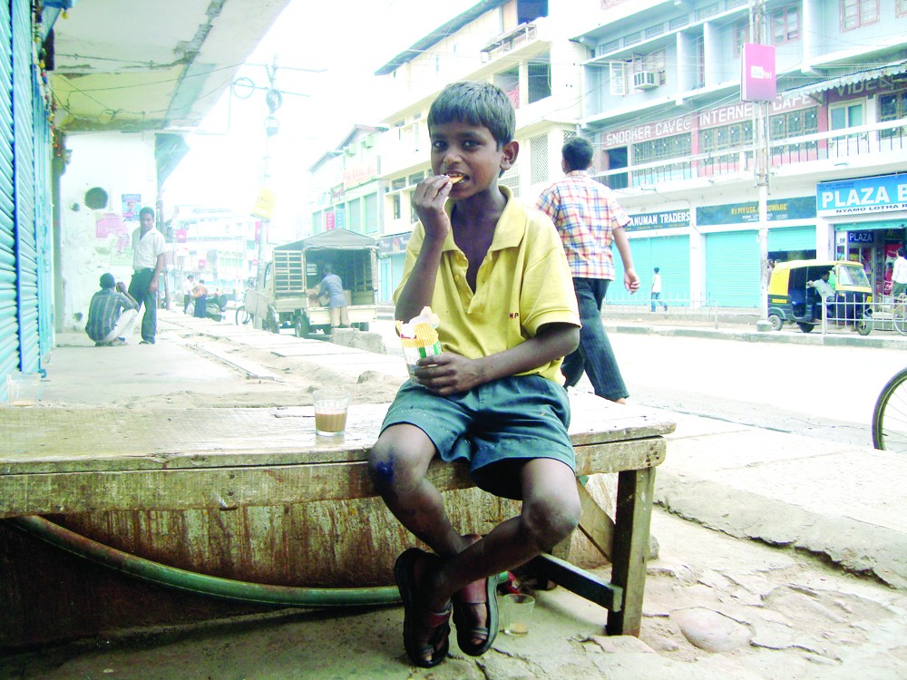 SIMPLE PLEASURES: A child labourer enjoys biscuits with tea from a stall in Church Road, Dimapur. (Morung File Photo)